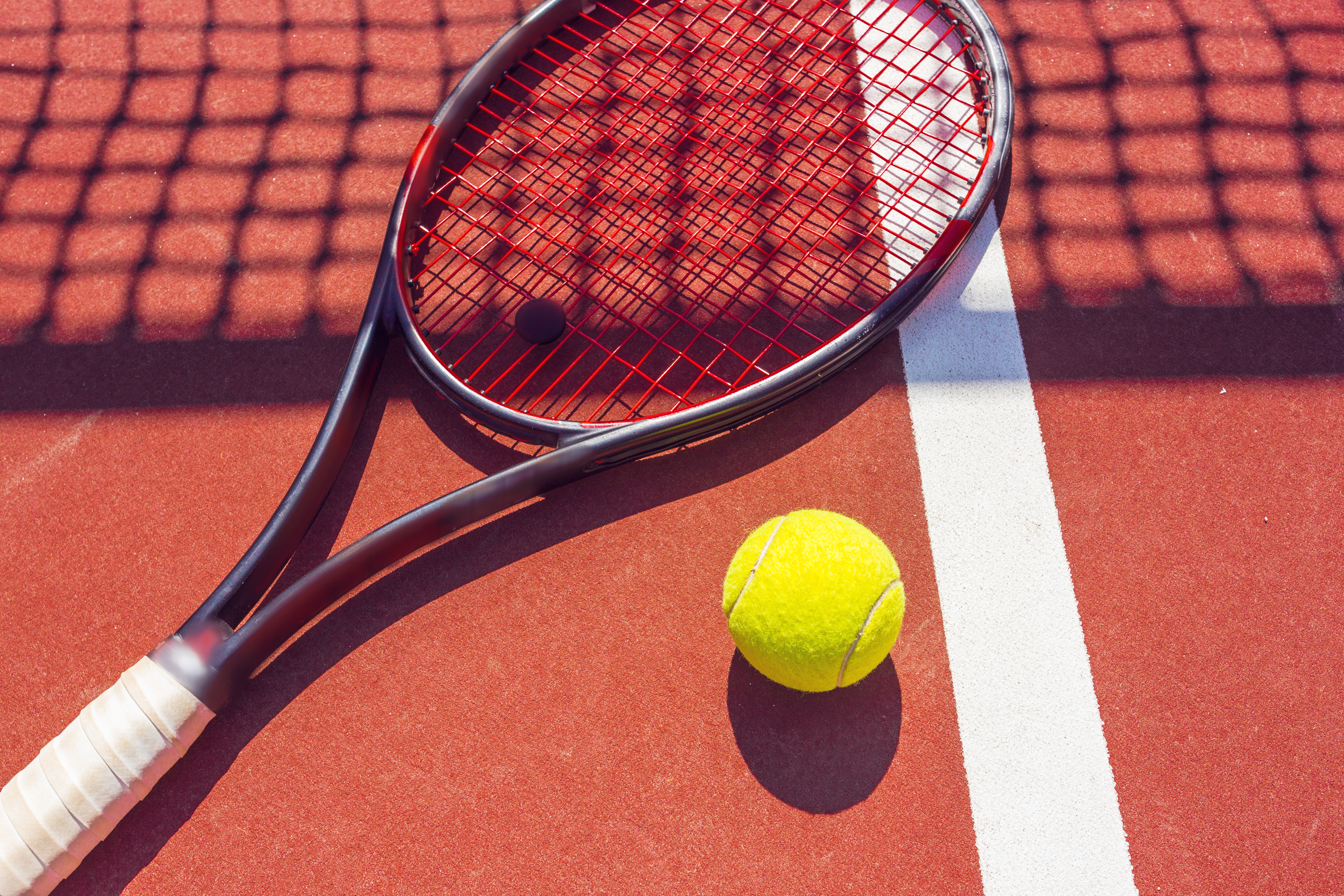 Photo d’une raquette et d’une balle de tennis sur un court rouge